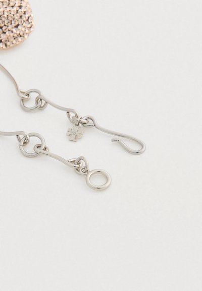 Ασημένια κλειδώματα βραχιολιού με ένα μικρό charm σε σχήμα παζλ που διαθέτει ένα μικρό διαφανές πολύτιμο λίθο, σε απλό λευκό φόντο.