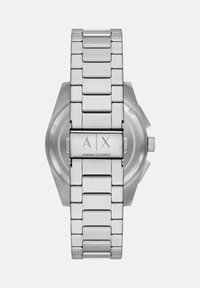 Kovinska ročna ura iz nerjavečega jekla s šestkotno ohišjem in brušenim zaključkom, ki ima zapiralo vgravirano z "A|X" in "Armani Exchange."