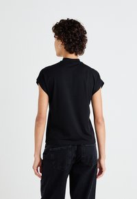 Svart kortärmad topp med hög krage, tillverkad av ett mjukt tyg. Baksidan har en enkel design med rak skärning.
