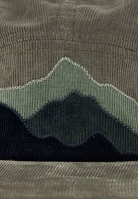 Kordelkappe in gedämpften Erdtönen, mit einem Wellenmuster in Grün und Marineblau. Texturiertes Gewebe mit sichtbaren Rippen und Nähakzenten.