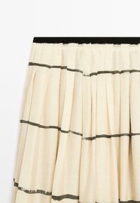 Jupe crème avec des plis verticaux, ornée de bandes noires horizontalement près du haut et du bas. Design simple et élégant, suspendue sur un fond blanc.