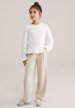 Haut blanc à manches longues texturé avec un ourlet à volants, associé à un pantalon large rayé beige et des baskets argentées. Tenue simple et décontractée.