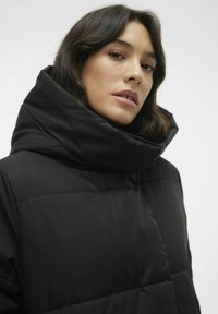 Manteau rembourré noir avec un col haut, doté d'une texture lisse et d'un motif matelassé. Conçu pour la chaleur et la protection.