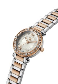 Reloj de acero inoxidable redondo con acentos en oro rosa, un bisel adornado con cristales y una esfera plateada que presenta números romanos y un patrón de rayos de sol.