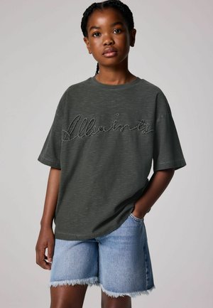T-paita tummanvihreä oversized-malli, jossa on brodeerattu "AllSaints" -logo, yhdistettyinä vaaleansinisiin farkkushortseihin, joissa on risareunus.