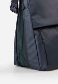 Navyfarbener Rucksack mit einer glatten, matten Oberfläche, Reißverschluss und einem Netzfutter, das durch eine teilweise geöffnete Seitentasche sichtbar ist.