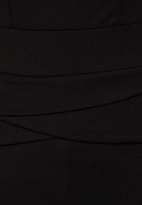 Černé šaty s texturovanou látkou, vodorovnými záhyby a detaily v zavinovacím stylu. Hladká, přiléhavá silueta s matným povrchem.