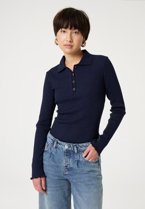 Marineblaues Langarm-Polohemd mit geripptem Stoff und einem Kragen, ausgestattet mit herzförmigen Knöpfen. Kombiniert mit hellblauen, locker sitzenden Jeans.