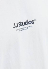 White cotton t-shirt featuring a black logo "JJ Studios" and additional text below, stitched in a simple, clear font, with a smooth texture.