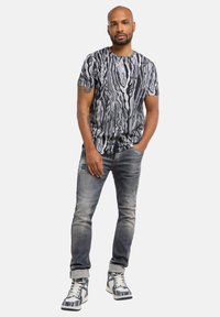 Graphic black and white t-shirt with abstract swirling patterns, paired with light gray distressed jeans and high-top sneakers with a patterned design.