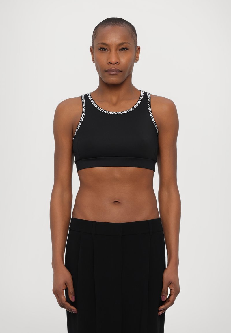 Black sports bra featuring a seamless design and contrast white logo trim along the neckline and armholes, paired with high-waisted black trousers.
