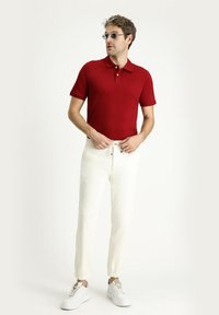 Polo shirt rosso a maniche corte, in tessuto morbido, abbinato a pantaloni jogger color crema con polsini elastici. Sneakers bianche completano il look.