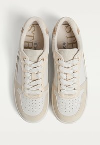 Sneaker beige con tomaia in pelle liscia e dettagli testurizzati. Presentano una punta perforata, lacci bianchi e un collare a costine.