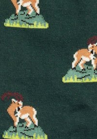 Donkergroen gebreide stof met herhaalde kleine motieven van bruine en witte berggeiten die op groene rotsen en gras staan.