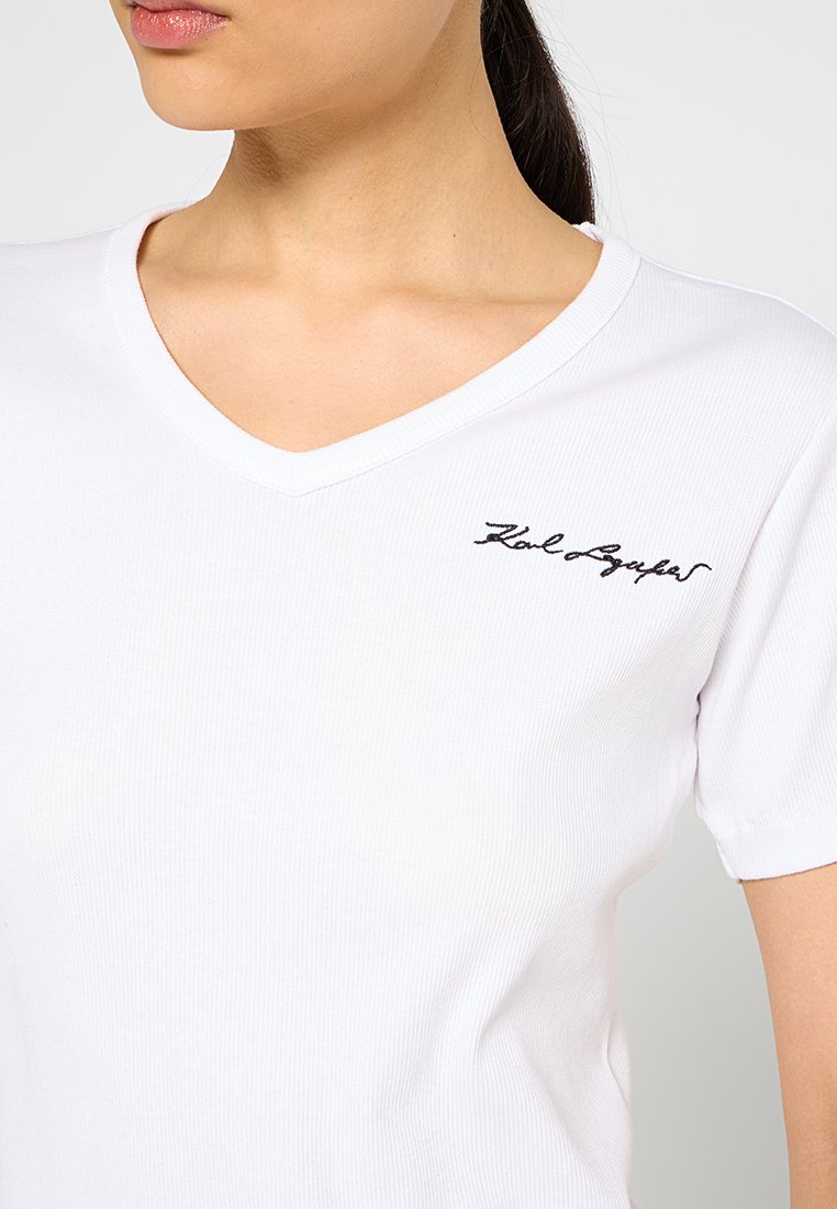 Biała koszulka typu V-neck wykonana z prążkowanej tkaniny, z małym czarnym haftowanym logo na piersi. Krótkie rękawy i dopasowany krój.