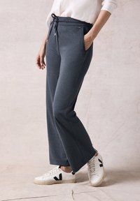 Dunkelgraue Sweatpants mit einem Kordelzugbund, Seitentaschen und einer lockeren Passform, kombiniert mit weißen Sneakern mit schwarzen Akzenten.