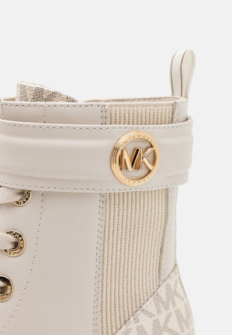 Bottine beige avec un panneau en velours côtelé texturé et du cuir lisse. Accent du logo doré MK sur la sangle ; design à lacets avec des œillets en métal.