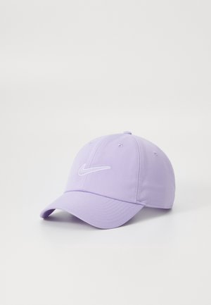 Casquette de baseball Nike violet clair avec une visière incurvée et un logo swoosh brodé blanc à l'avant, posée sur une surface blanche.