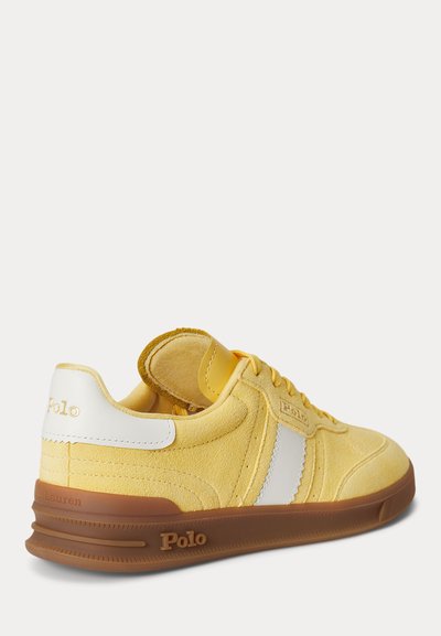 Κίτρινο sneaker Polo Ralph Lauren με λευκή ετικέτα στη φτέρνα, λευκή πλαϊνή ρίγα, καφέ σόλα και ανάγλυφο λογότυπο Polo στη σόλα και τη φτέρνα.