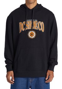 Svart huvtröja med framficka, med orange text "DCSHOECO" och logotyp i mitten. Bomullsblandning, avslappnad design.