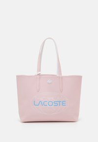 Sac fourre-tout rose en matériau texturé avec logo "LACOSTE" bleu et motif carte du monde, avec poignées blanches et fermeture éclair.