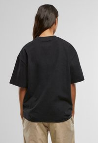 Fekete, oversized pamut póló rövid ujjakkal, kerek nyakkivágással és sima hátoldali dizájnnal. Lazán illeszkedő, minimális részletezéssel.