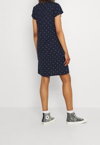 Robe bleu marine à manches courtes avec des pois blancs, associée à des baskets montantes à motifs noirs et blancs. Design simple, longueur au-dessus du genou.