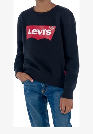 Czarna bluza z kapturem z czerwonym logo Levi's na przodzie. Materiał jest miękki, z żebrowanymi mankietami i dołem. Noszona z niebieskimi dżinsami.