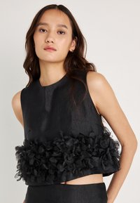 Top preto sem mangas com um corpete texturizado e um detalhe de tecido com babados na bainha, confeccionado em um material leve.