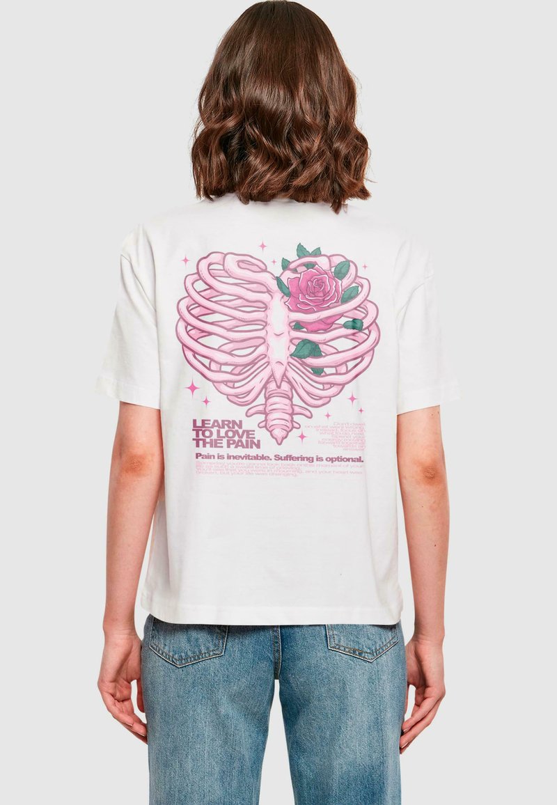 Hvit T-skjorte med grafikk av et rosa ribbein og en rose. Teksten lyder "Lær å elske smerten. Smerte er uunngåelig. Lidelse er valgfritt."