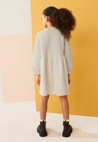 Vaaleanharmaa mekko, jossa on muotoiltu olkapää ja sileä hame, polven ylle. Yhdistetty mustiin nilkkureihin, joissa on helmiripustuksia.