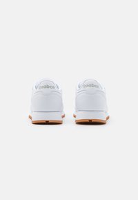 Białe sneakersy z gładką syntetyczną cholewką, z wyściółką w kołnierzu, gumową podeszwą i detalem logo na pięcie.