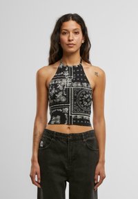 Mustmust halsika crop top, mille on valged paisleide ja geomeetrilised mustrid, valmistatud kergest kangast, paaritatud tumedate teksadega.