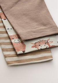 Set of three children's T-shirts: one brown solid, one light cream with cow design, and one beige striped pattern. Soft cotton fabric.