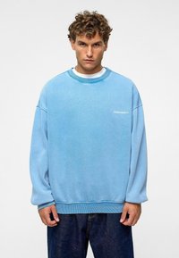 Lichtblauwe sweatshirt gemaakt van zachte stof, met een ronde halslijn en een losse pasvorm. De voorkant heeft een klein wit logo op de borst.