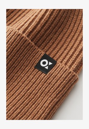 Brown knitted beanie hat with ribbed texture, featuring a black label with white logo detail sewn on the cuff.