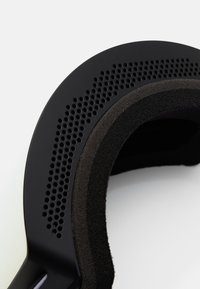 Cuffia nera con un archetto texturizzato e imbottito all'interno, e una serie di piccole perforazioni lungo il bordo esterno.