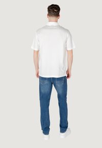 Polo bianco a maniche corte abbinato a jeans blu medio, caratterizzato da una vestibilità rilassata e una linea dritta tipica dell'abbigliamento casual.