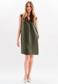 Luźna oliwkowozielona sukienka z krótkimi rękawami i dekoltem w kształcie litery V, wykonana z fakturowanej tkaniny, z bocznymi kieszeniami i długości do kolan.