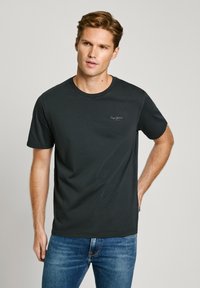 Camiseta de algodón negra de manga corta con cuello redondo, que presenta un pequeño logo en el pecho y una textura suave. Combinada con unos vaqueros de denim azul.