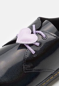 Scarpa in pelle verniciata nera con finitura lucida, presenta lacci intrecciati viola, un fermalacci a forma di cuore e occhielli neri.