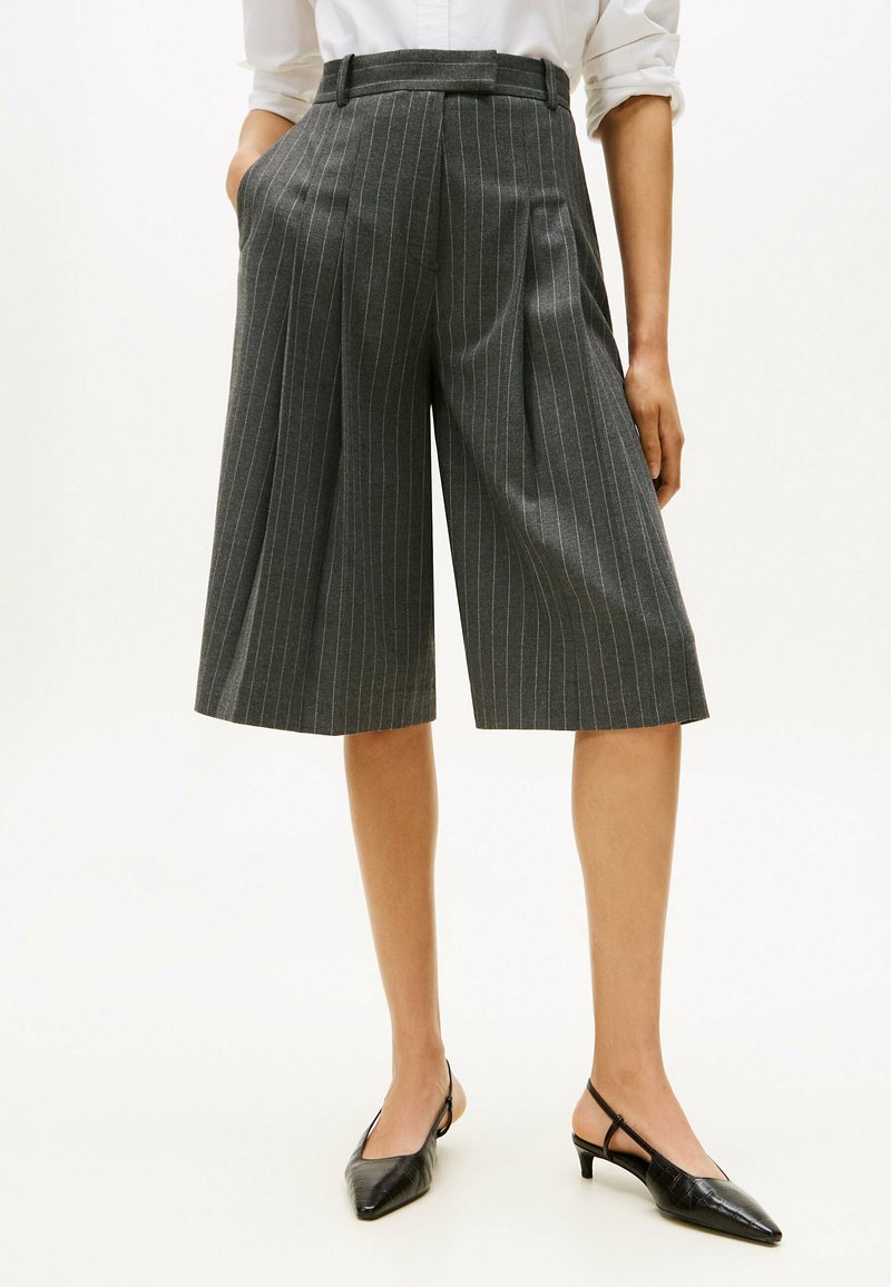 Pantalones culottes a rayas grises con cintura alta, plisados y bolsillos laterales. Se combinan con zapatos de tacón negro con punta alargada para crear un contraste.