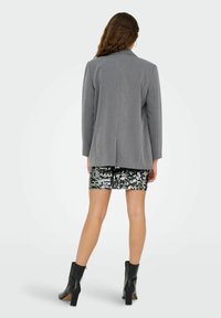 Pelēks žakets ar pielāgotu dizainu, garām piedurknēm un vienu atvērumu aizmugurē, savienots ar melnu spīguļotu mini svārku un melniem potīšu zābakiem.