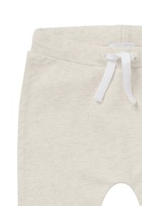 Lichtbeige katoenen joggingbroek met elastische tailleband, witte trekkoord en een ronde uitsparing bij de knie. Zachte textuur, minimalistisch ontwerp.