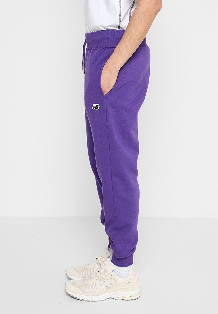Pantaloni della tuta viola realizzati in tessuto morbido, con vita elastica, tasche laterali e un piccolo logo nero sul davanti.