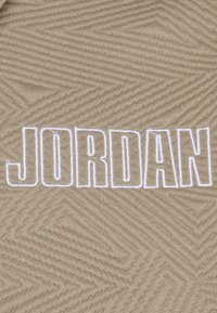 Rudos audinio zigonometryje su tekstūriniu zigzagų raštu; aprašytas ryškiu baltu siuvinėjimu "JORDAN".