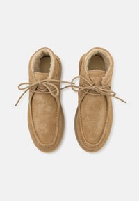 Καφέ σουέτ ankle μποτάκια με απαλό κρεμ χρώμα εσωτερικά, διαθέτουν στρογγυλή μύτη, δέσιμο με κορδόνια και διακοσμητική ραφή κατά μήκος της σόλας.