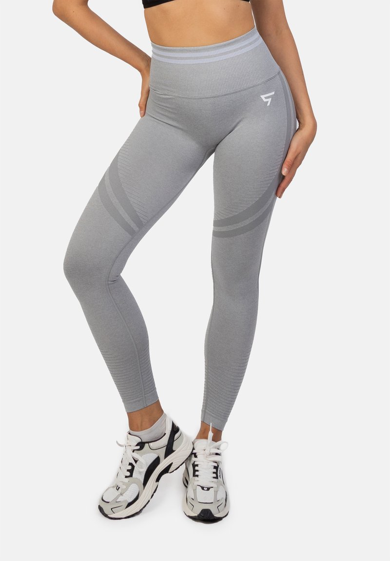 Szare legginsy z wysokim stanem o prążkowanej fakturze, z dwoma poziomymi paskami i logo na udzie. W zestawie z jasnymi sneakersami.