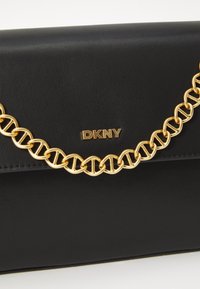 Borsa a mano in pelle nera con tracolla a catena dorata, che presenta un logo DKNY. Ha una superficie liscia e un design strutturato.
