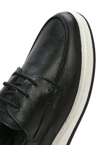 Scarpa nera in pelle con finitura testurizzata, punta arrotondata, design con lacci e suola in gomma bianca con bordo testurizzato.
